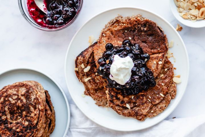 Greek yogurt and flax pancakes on a plate with blueberry compote, whipped cream, and almonds.