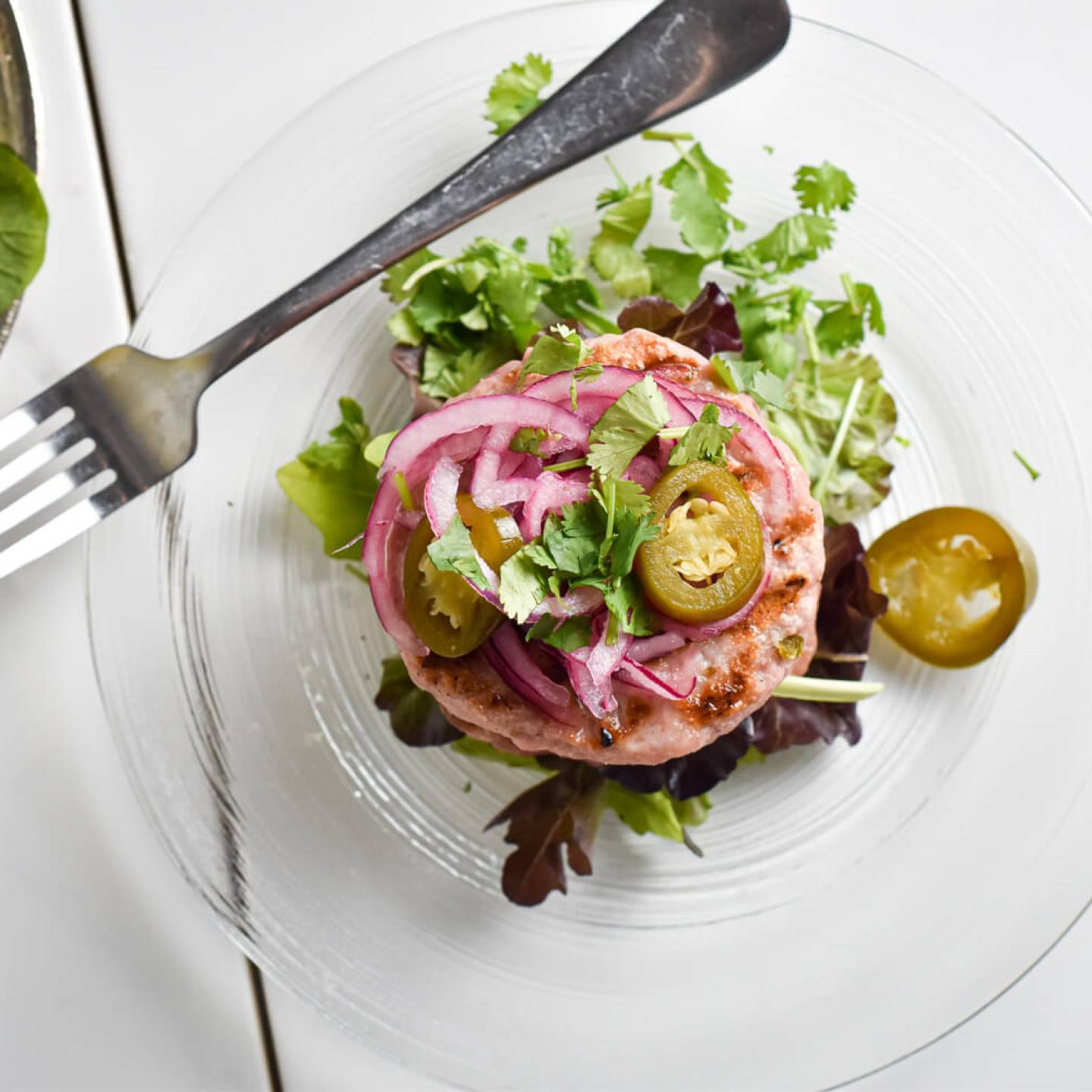 Green chile turkey burger with pickled red onions and greens on a plate with pickled jalapenos.