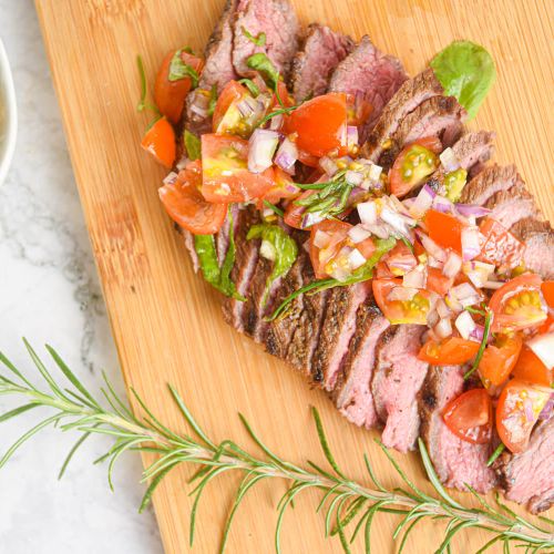 Grilled steak on a wooden board with tomato, and basil salad.