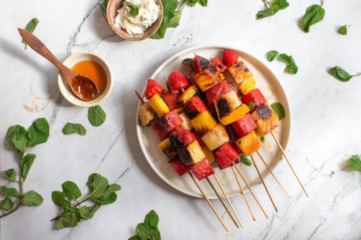 Grilled fruit kabobs with banana, watermelon, strawberries, and mango on wooden skewers with honey and mint.