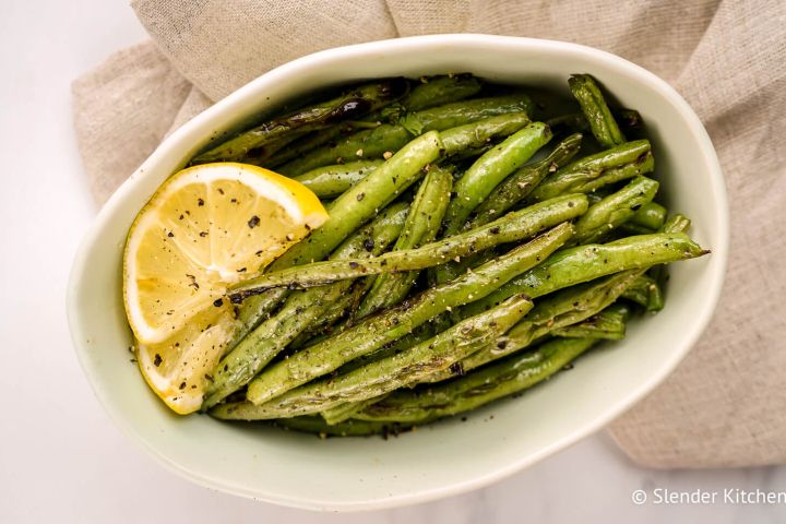 Grilled green beans served on a plate with fresh lemon, salt, and pepper.