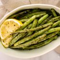 Grilled green beans served on a plate with fresh lemon, salt, and pepper.