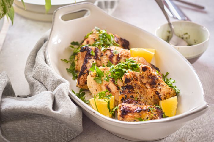 Grilled lemon dijon chicken thighs with fresh lemon and parsley in a white dish with a linen napkin.