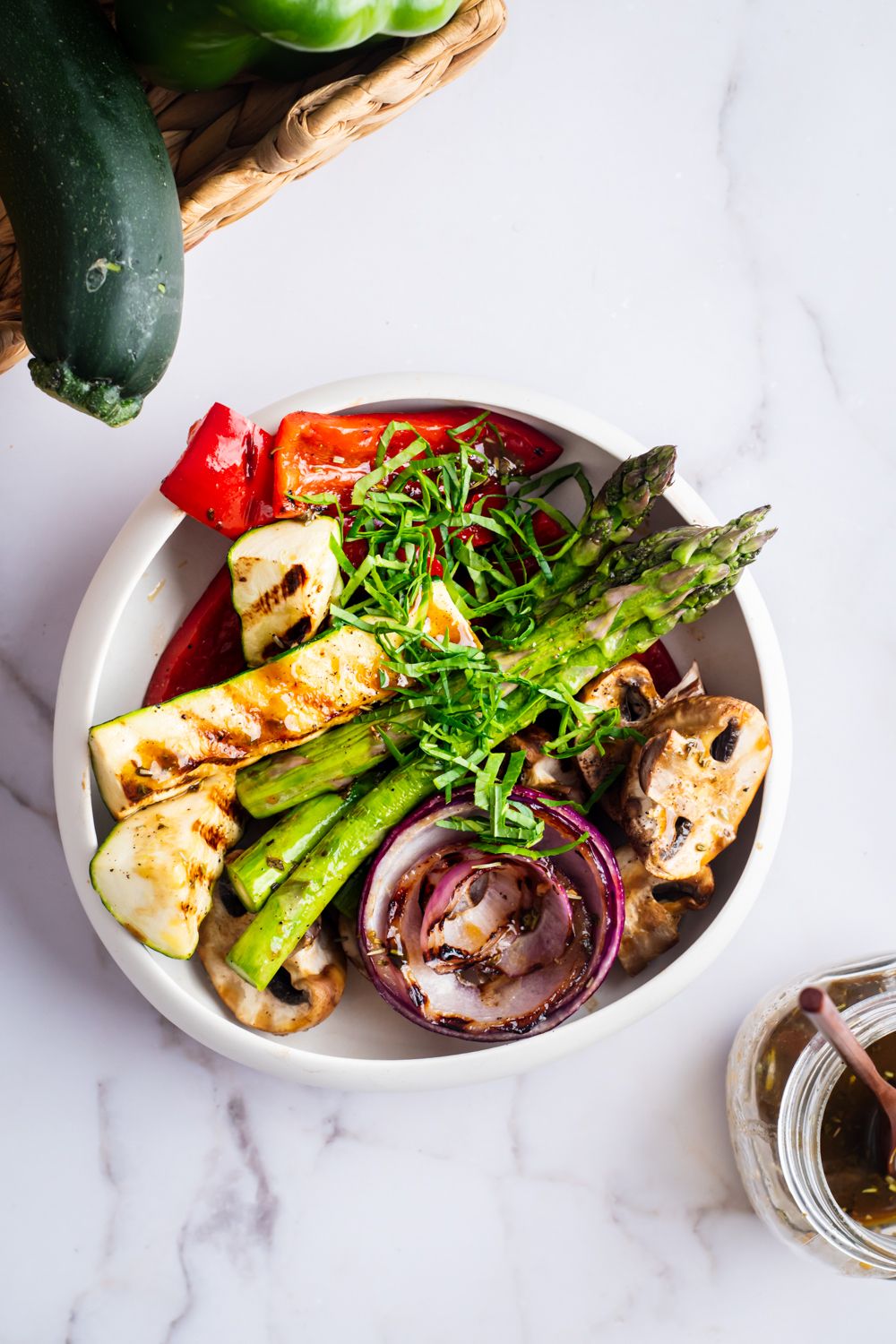 Marinated grilled vegetables including onion, zucchini, bell peppers, and mushrooms in a bowl with fresh herbs and balsamic vinegar.