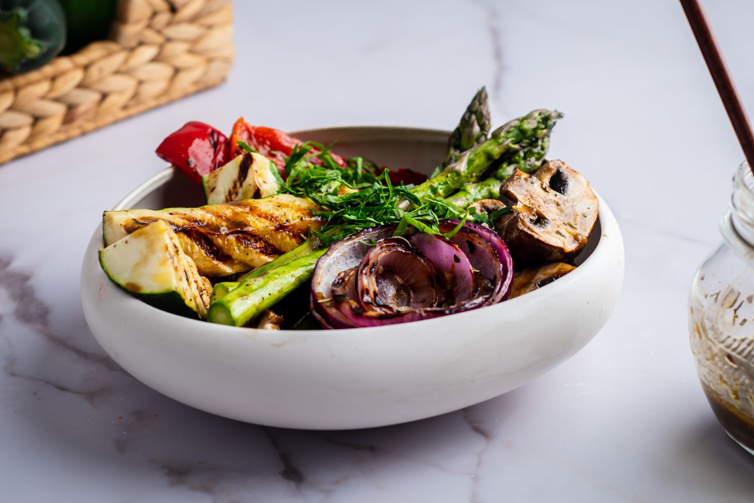 Grilled vegetables with balsamic marinade in a bowl with extra marinade on the side in a jar.