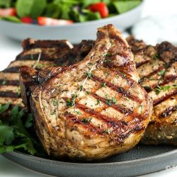 Grilled pork chops with grill marks and fresh thyme on a plate.