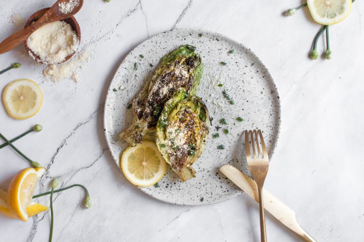 Grilled romaine lettuce on a plate with lemon, Parmesan, olive oil, and vinegar.