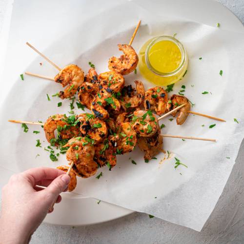 Grilled shrimp on wooden skewers with spices, lemon juice, and melted butter.