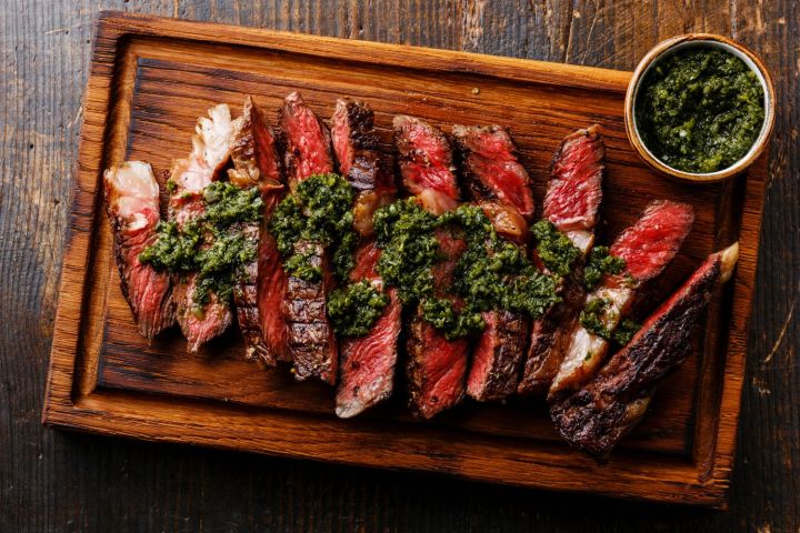 Grilled sirloin steak on a cutting board with chimichurri.