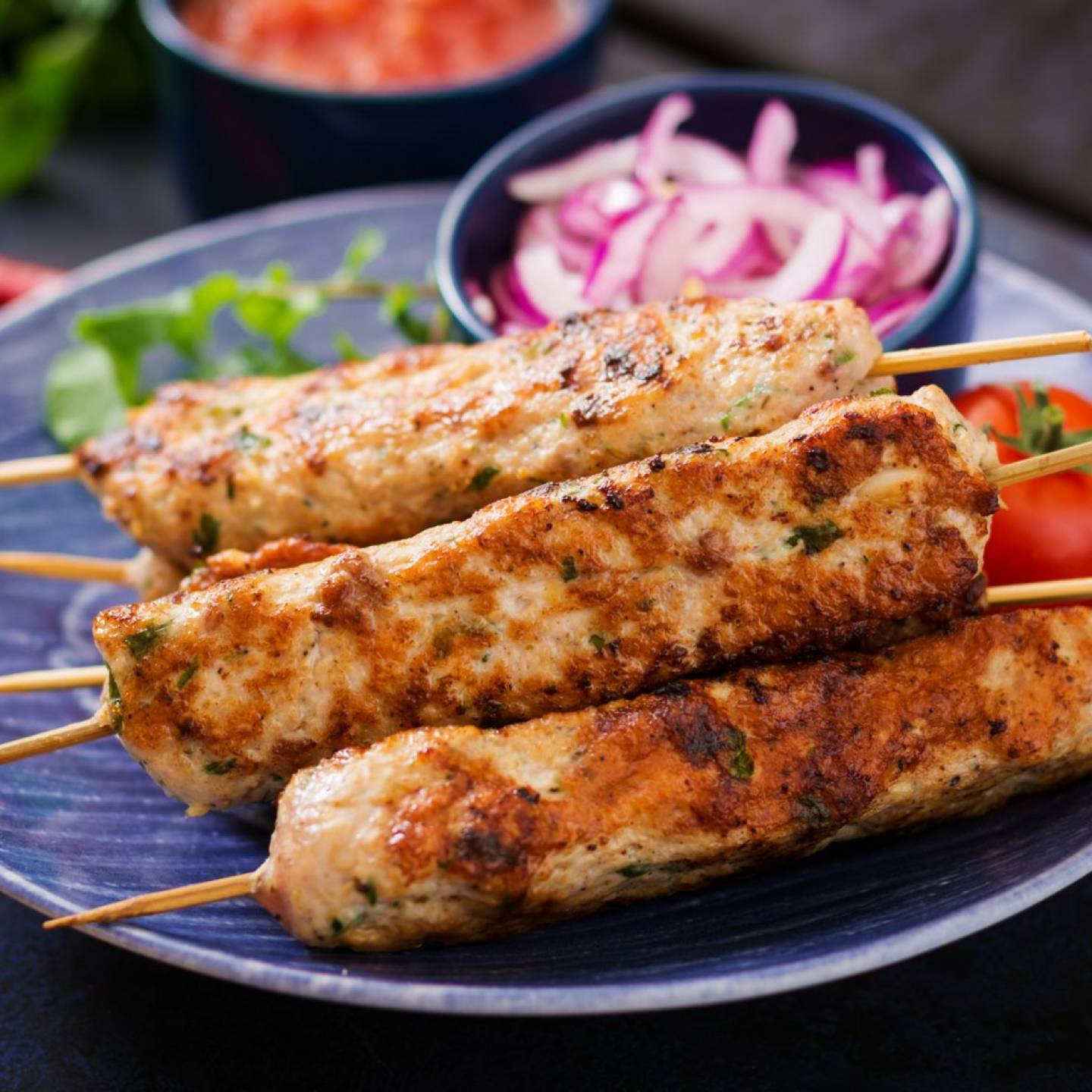 Grilled turkey lula kabobs with red onions, parsley, and lemon on a slate board.