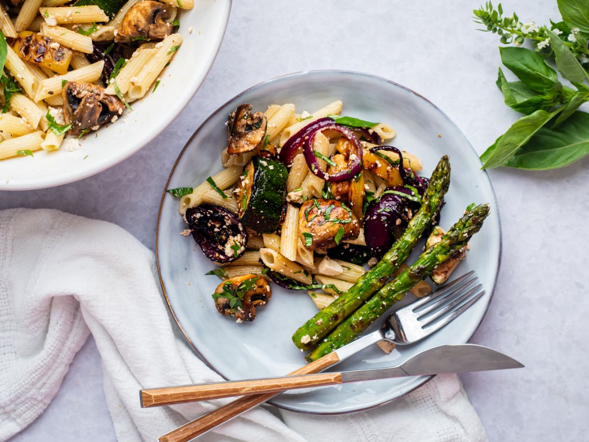 Grilled vegetable pasta salad with balsamic dressing, mushrooms, zucchini, asparagus, red onion, and herbs on a plate.