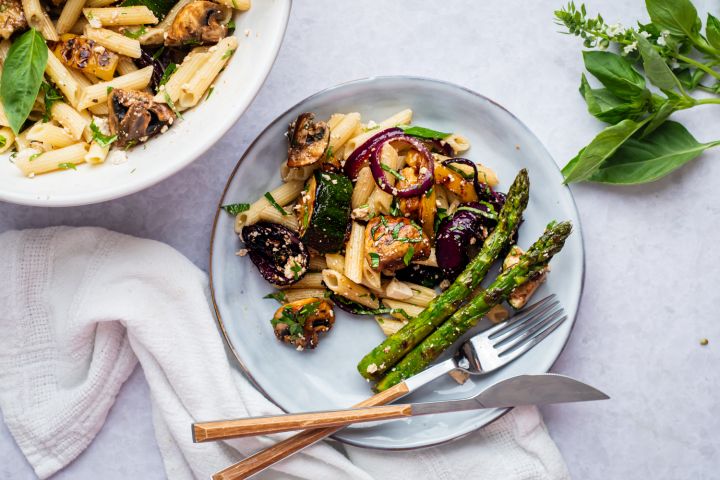 Grilled vegetable pasta salad with balsamic dressing, mushrooms, zucchini, asparagus, red onion, and herbs on a plate.