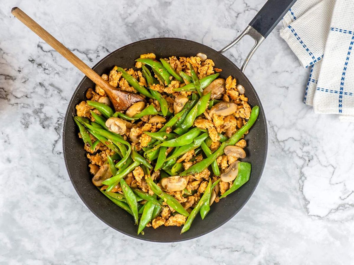 Ground Turkey stir fry with green beans and mushrooms in a black skillet with a wooden spoon.