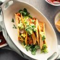 Ground turkey tacos in crispy baked tortillas with salsa, lettuce, radishes, and guacamole on a plate.