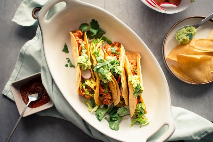 Ground turkey tacos in crispy baked tortillas with salsa, lettuce, radishes, and guacamole on a plate.