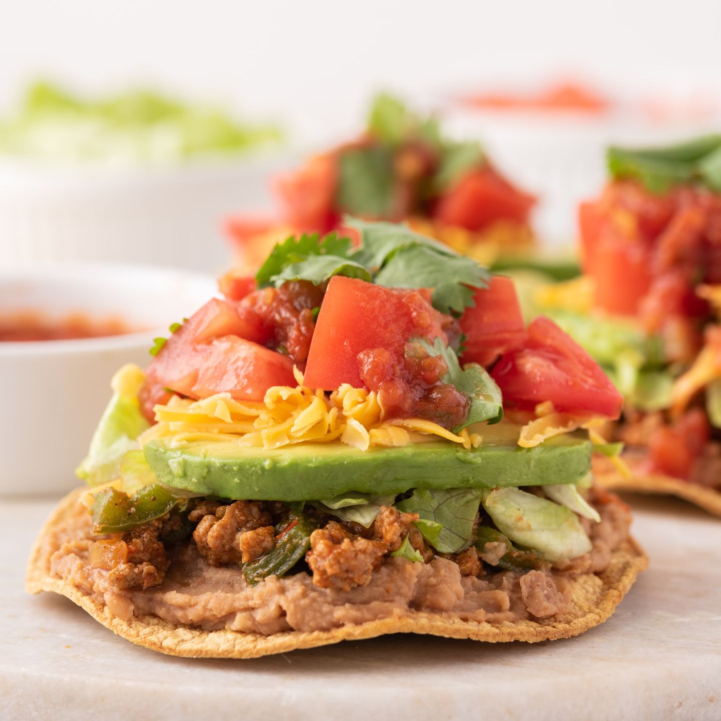 Ground turkey tostadas with refried beans, ground turkey, lettuce, tomato, avocado, and shredded cheese.