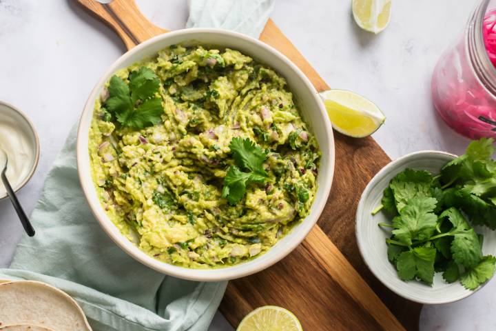 Guacamole with mashed avocados, cilantro, red onion, jalapeno, lime juice, salt, and pepper in a bowl.