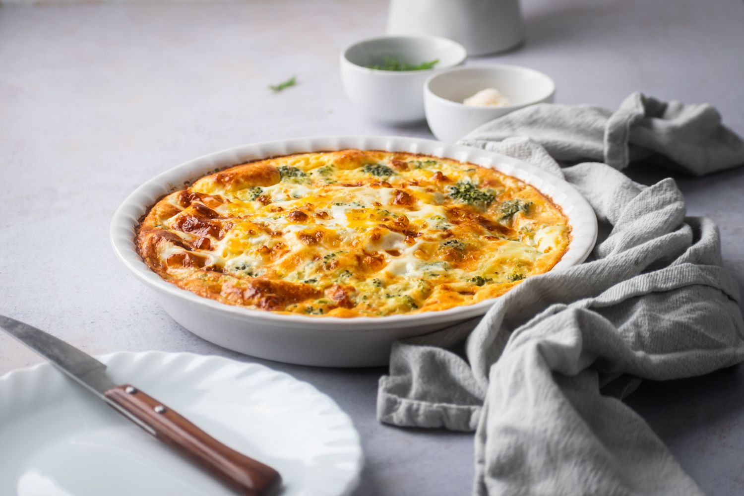 Ham frittata with cheese and broccoli in a white baking dish with a blue napkin.