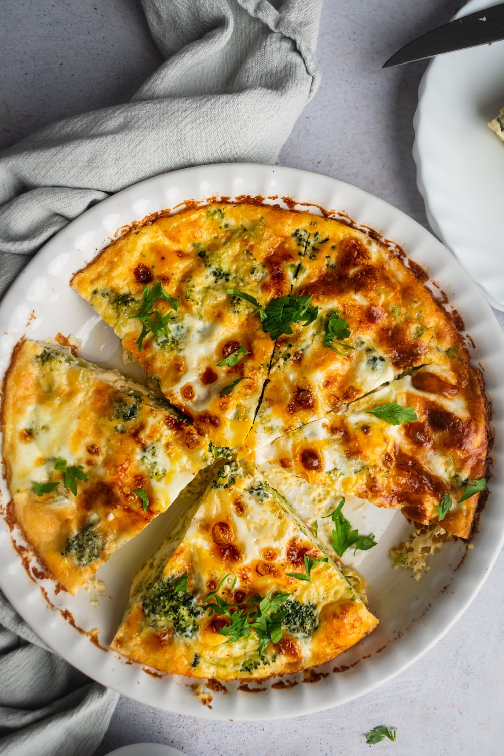 Baked egg frittata with ham, cheese, and broccoli cut into slices in a white pie plate.