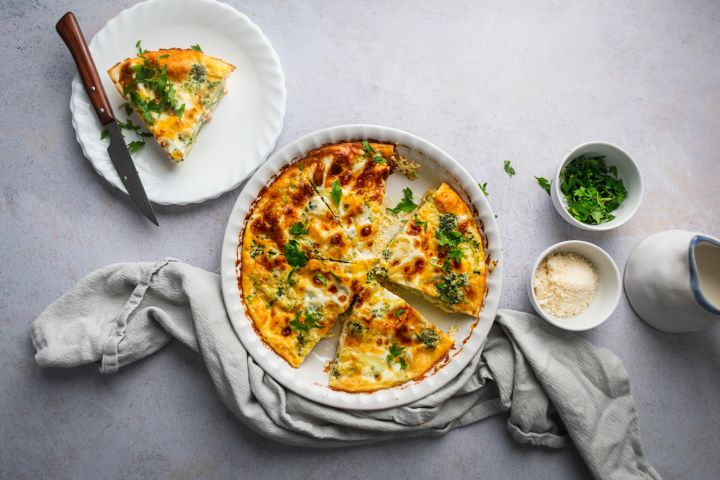 Ham and cheese frittata with broccoli cooked in a pie dish with a slice cut on the side. 