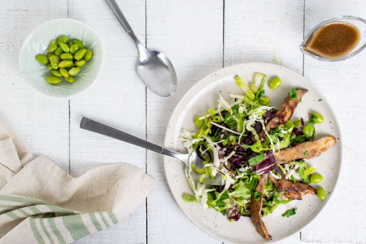 Chinese Chicken Salad with sesame dressing, chicken, edamame, and cabbage on a plate with a fork and spoon.