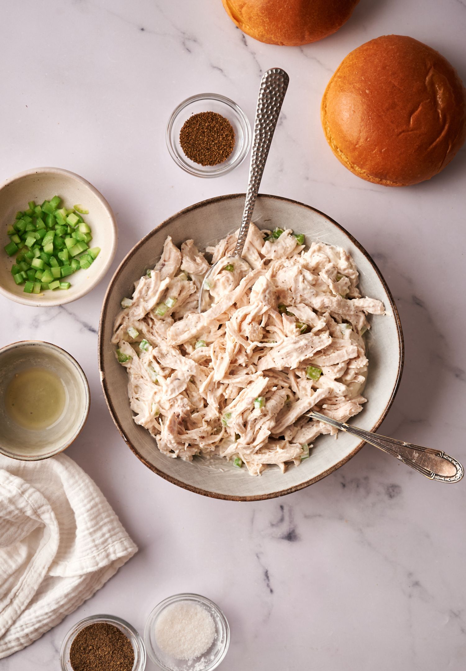 Healthier chicken salad served in a bowl with shredded chicken, celery, yogurt, and spices with rolls on the side.