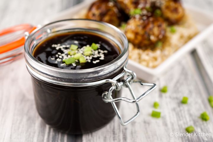 Homemade teriyaki sauce in a jar with teriyaki chicken meatballs in the background.