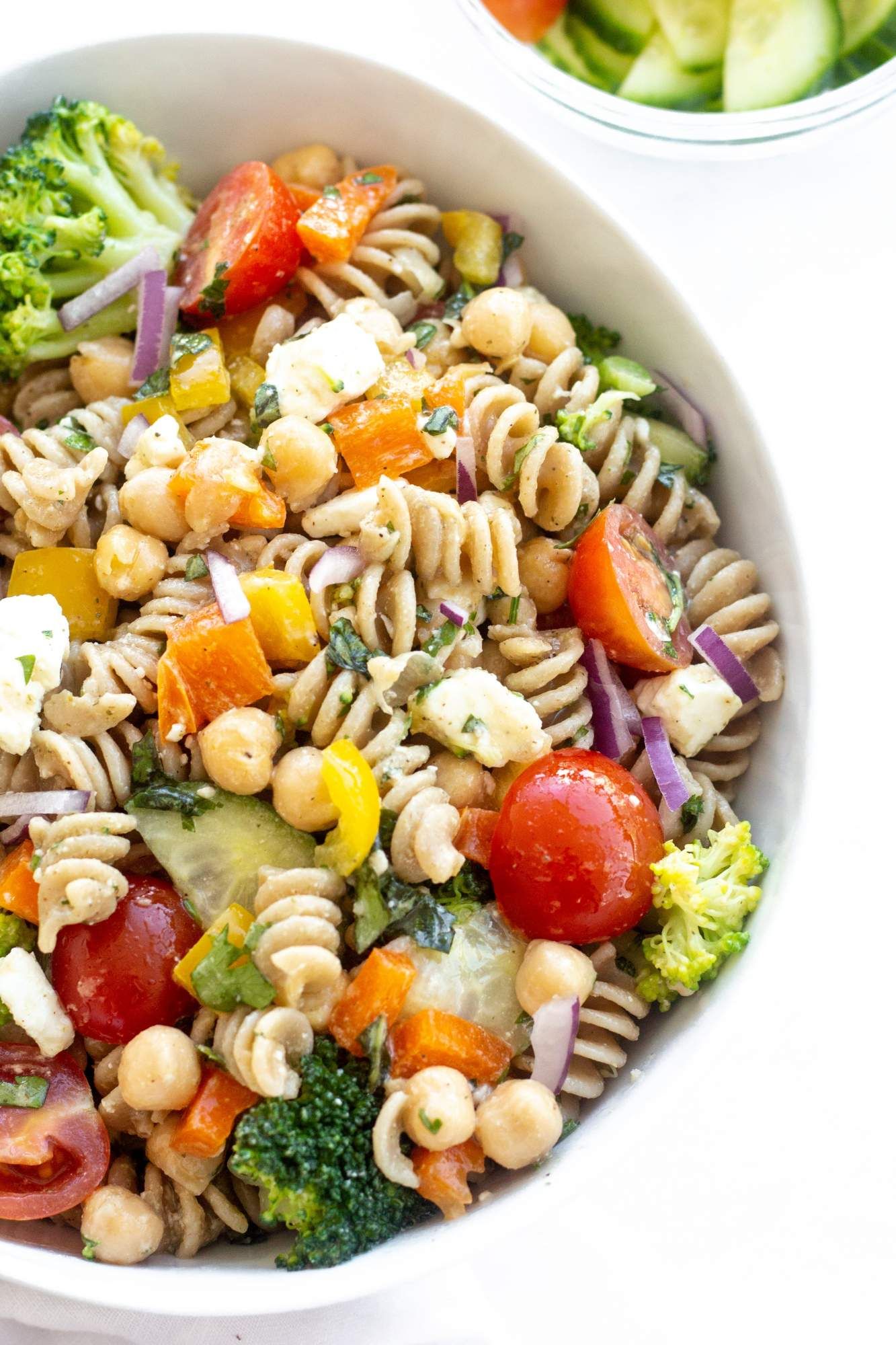 Healthy pasta salad with chickpeas, feta cheese, chopped vegetables, and a lemon dressing in a white bowl with fresh herbs.