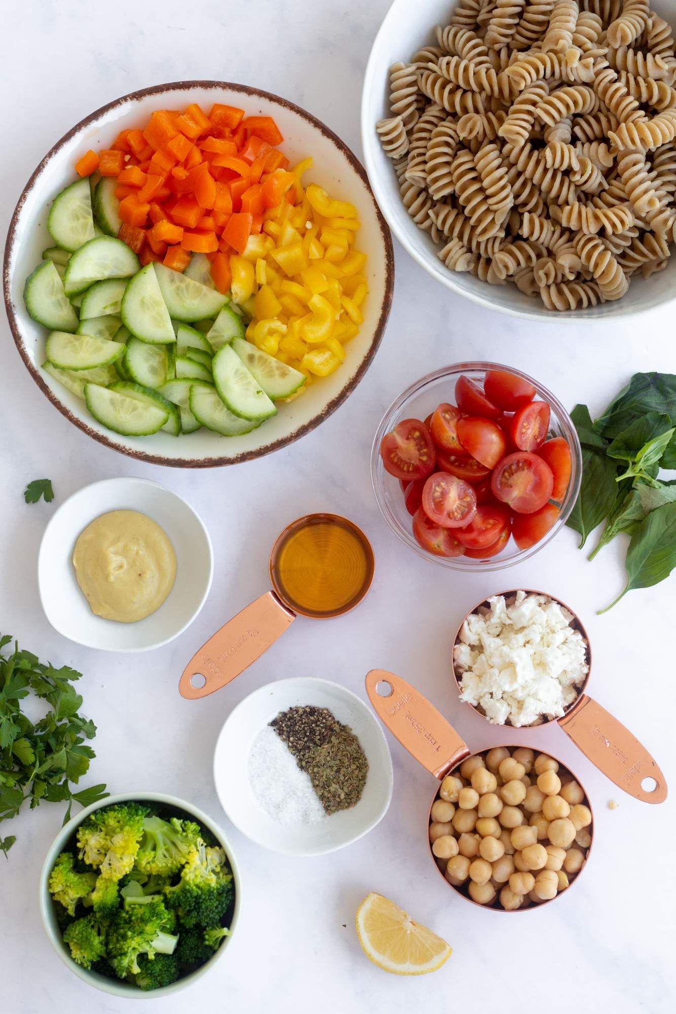 Ingredients for vegetable pasta salad including whole wheat pasta, cucumbers, bell peppers, tomatoes, feta cheese, and chickpeas.