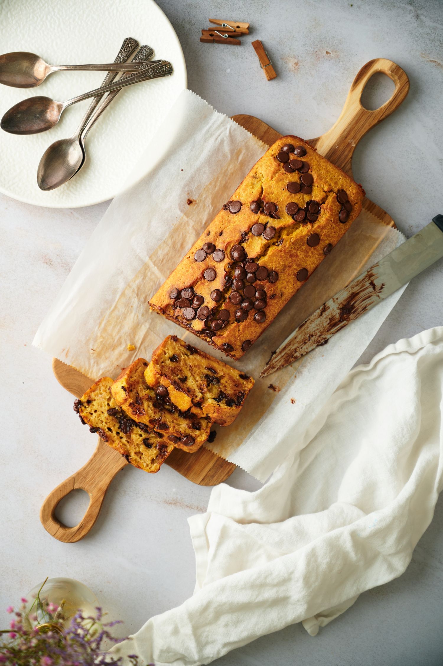 Sliced pumpkin bread with chocolate chips on a board with spoons on the side.