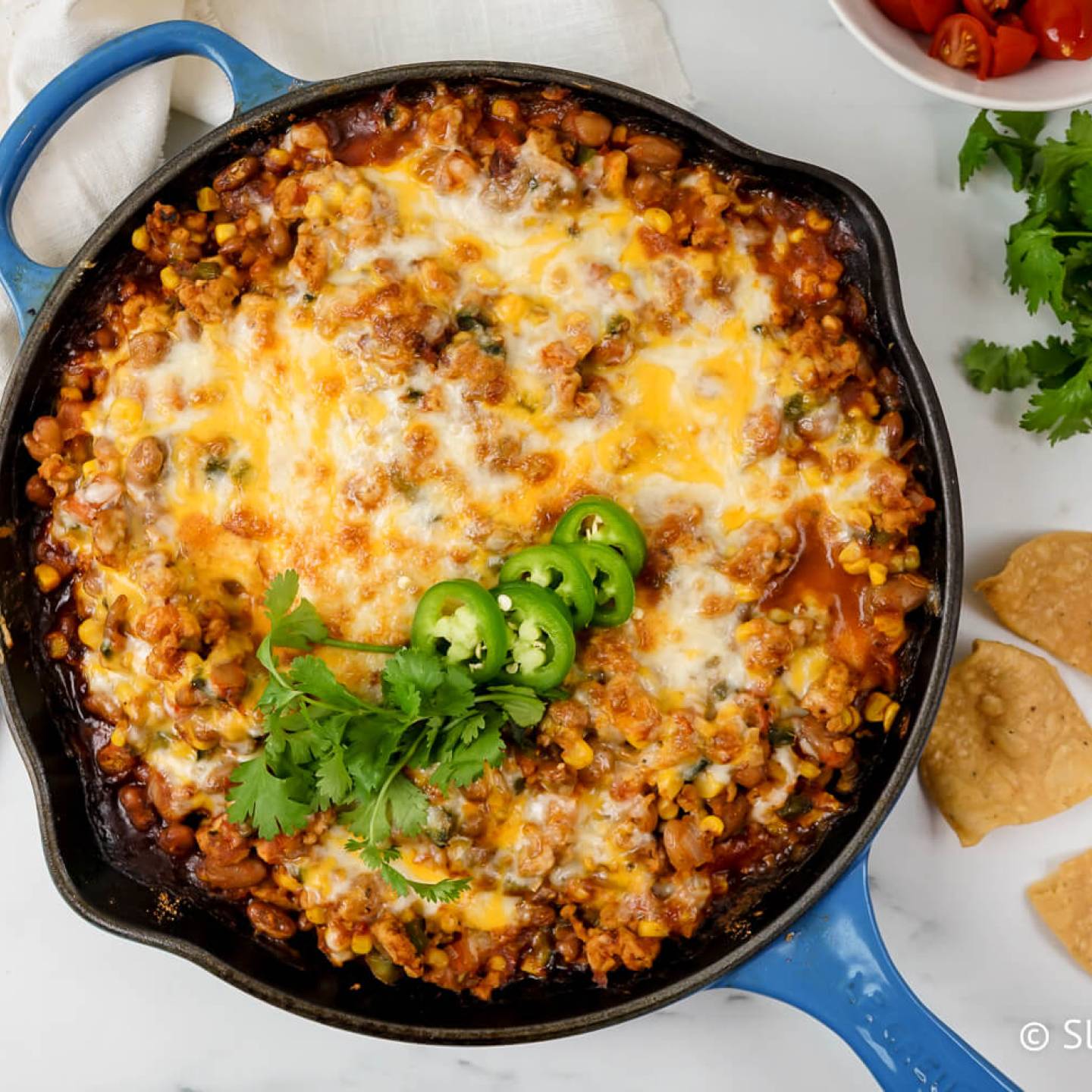 Taco casserole with pinto beans, onions, peppers, turkey, corn, salsa, and melted cheese with chips, cilantro, and jalapeno on the side.