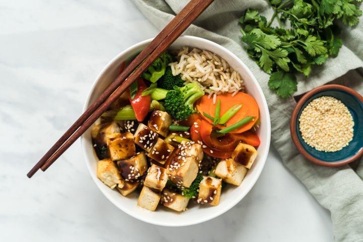 Hoisin tofu with broccoli, carrots, peppers, and green onions over brown rice with hoisin sauce drizzled on top.