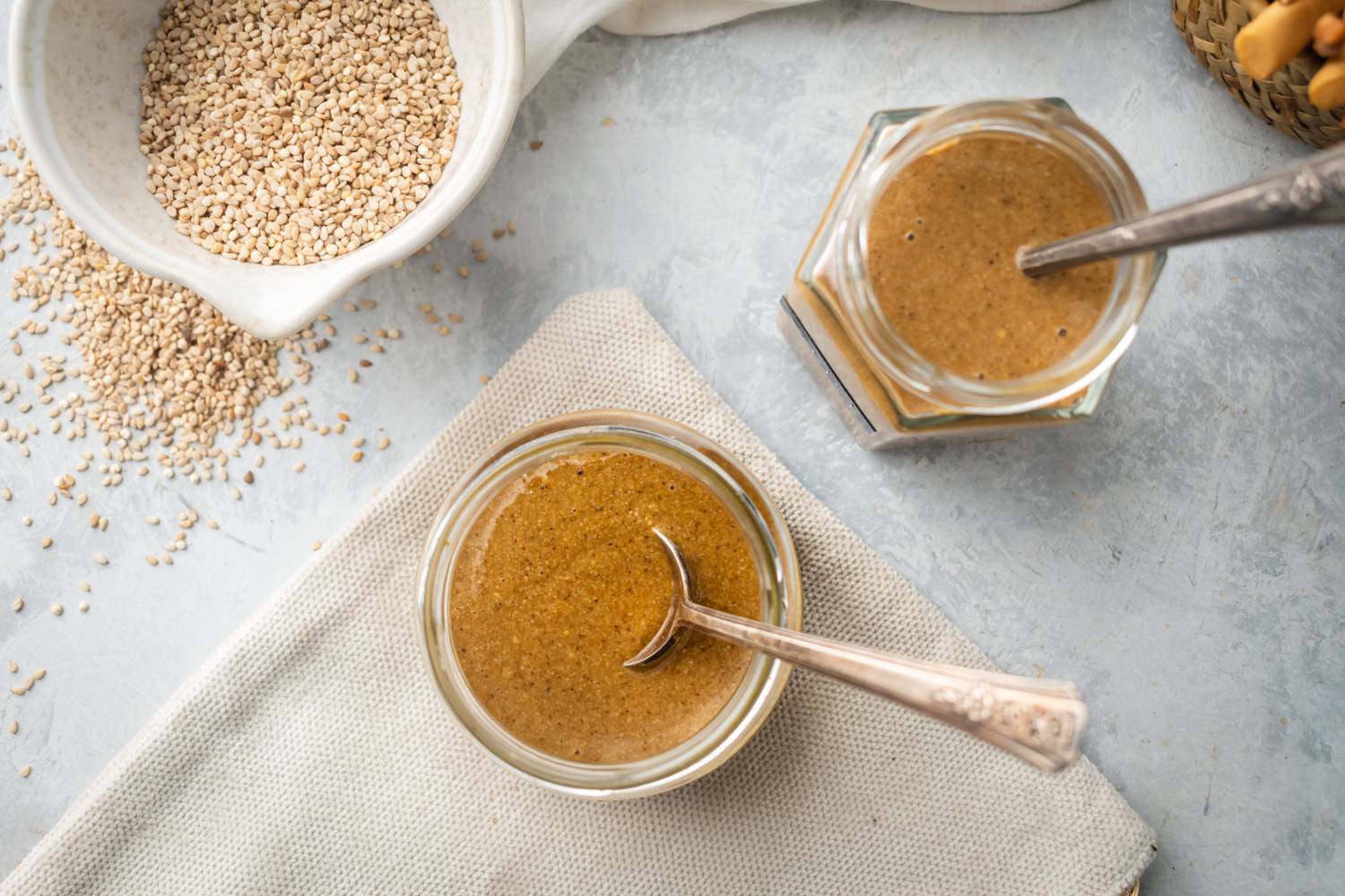 Homemade tahini with toasted sesame seeds and olive oil served in glass jars with spoons.