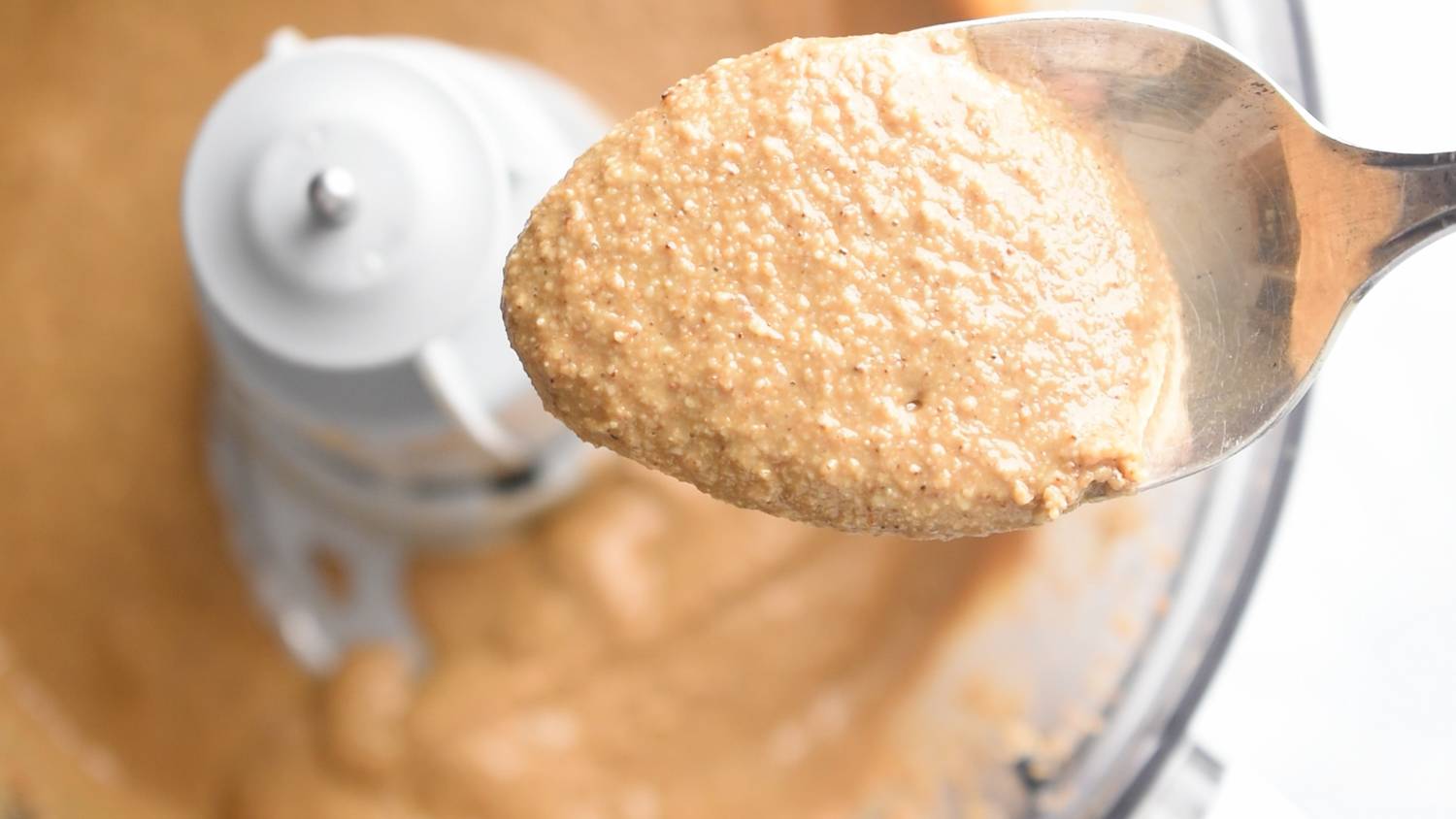 Spoonful of homemade tahini with a food processor in the background.