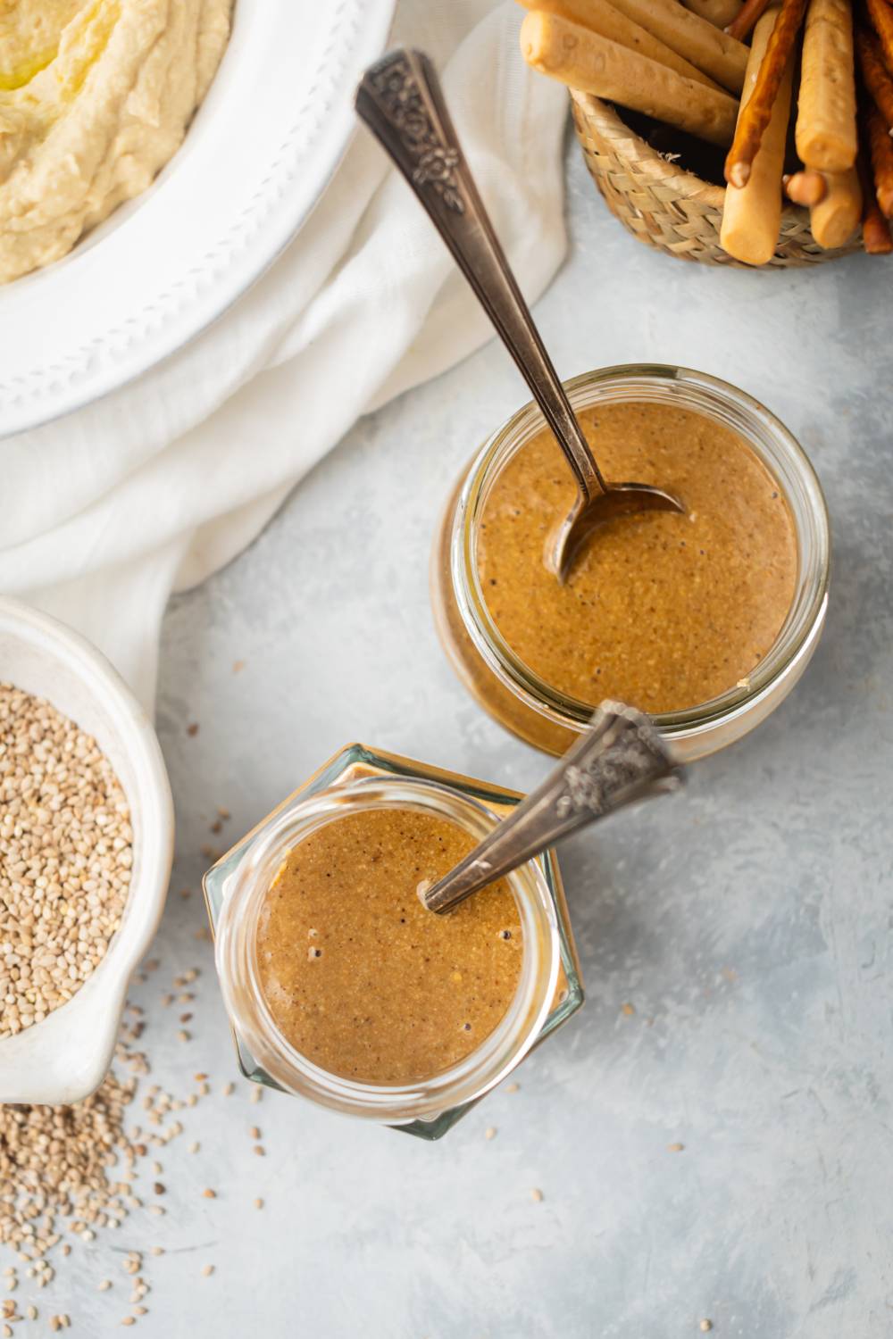 Sesame tahini stored in to glass jars with hummus and breadsticks on the side.