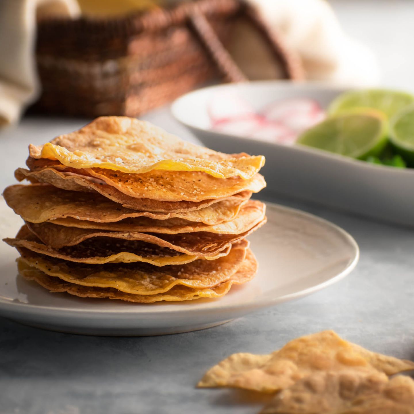 Homemade tostada shells with baked corn tortillas on a plate with limes, radishes, and cilantro on the side.