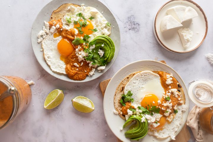 Huevos rancheros with sunny side up eggs served on corn tortillas with ranchero sauce, avocado, and cheese.