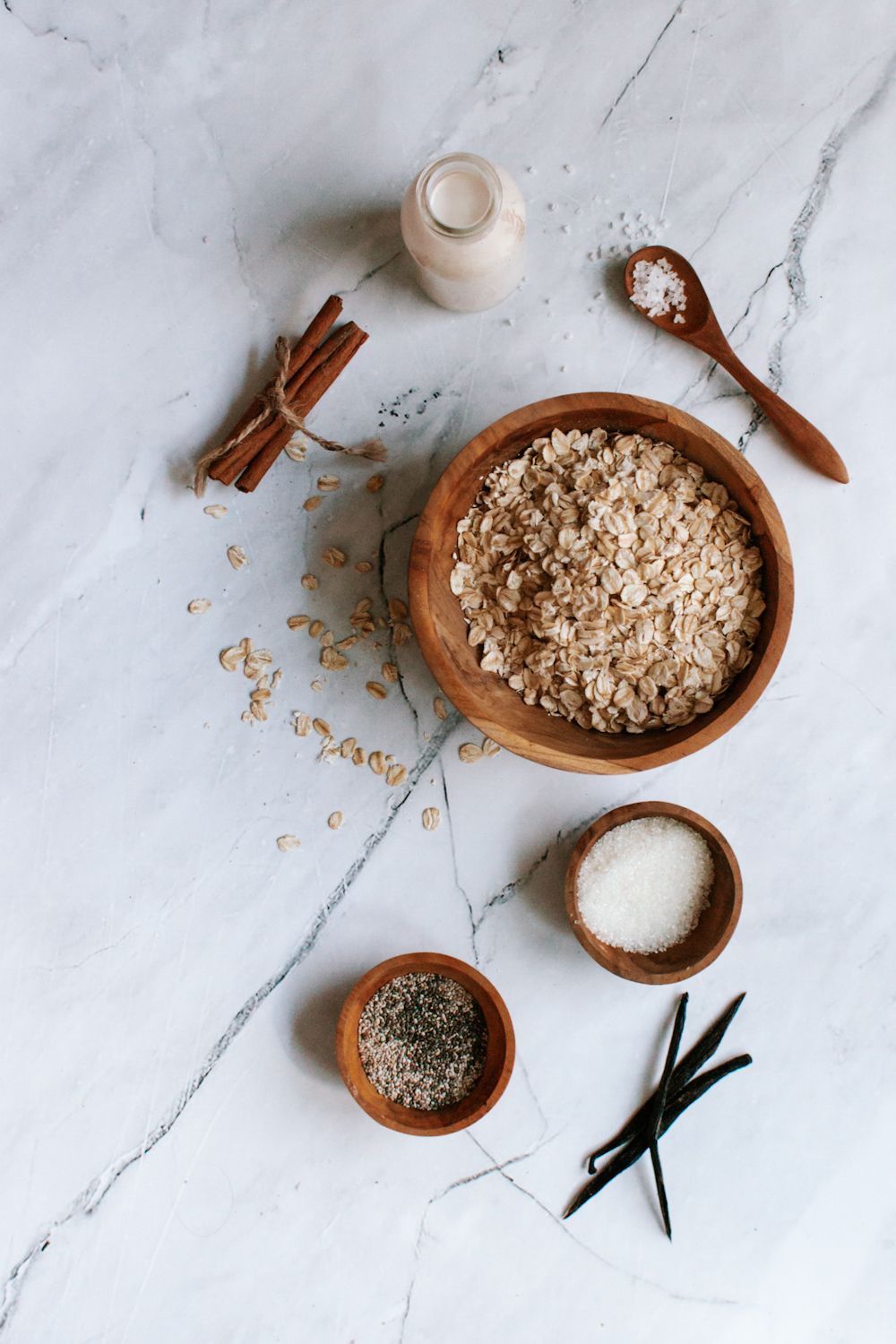 Overnight oatmeal ingredients on a marble board with rolled oats, cinnamon, almond milk, and chia seeds.