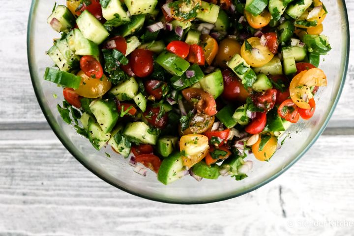 Israeli salad with cucumbers, tomatoes, red onion, parsley, and lemon dressing in a bowl.