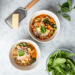 Italian bean and vegetable soup with cannellini beans, tomatoes, carrots, spinach, and zucchini in two bowls with Parmesan cheese.