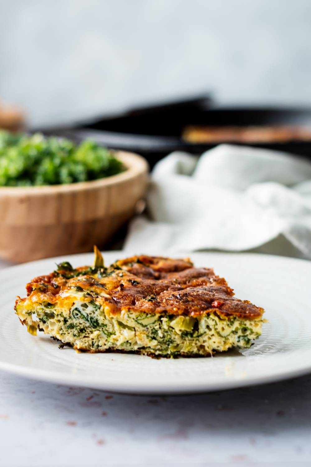 Frittata with kale, eggs, onions, cheddar cheese, and parmesan cheese sliced and served on a plate.