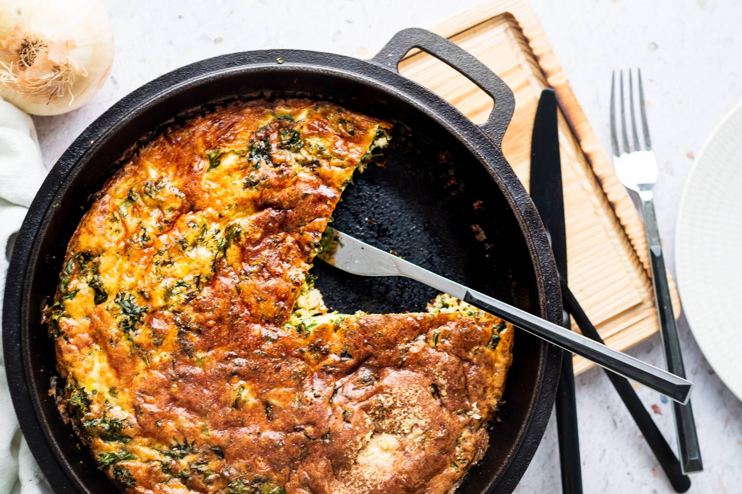 Baked kale frittata with melted cheese served in a cast iron skillet with a knife.