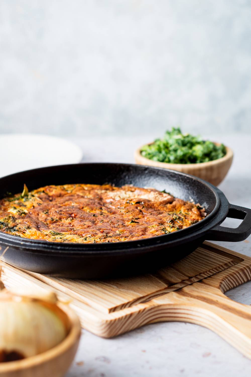 Kale and onion frittata in a cast iron skillet with melted cheddar and Parmesan cheese.