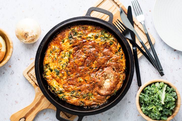 Kale frittata with onions, cheddar cheese, Parmesan cheese, and sauteed kale in a cast iron skillet.