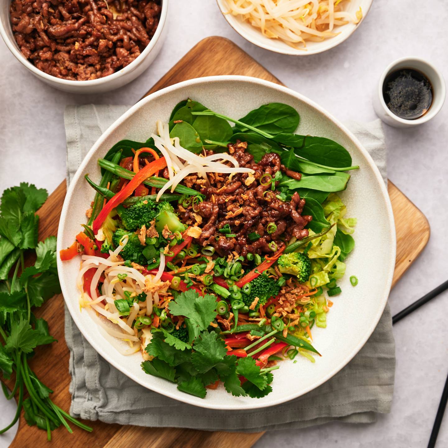 Korean beef bowls with rice, cilantro, carrots, bell peppers, and sprouts in a bowl with spicy sauce. 