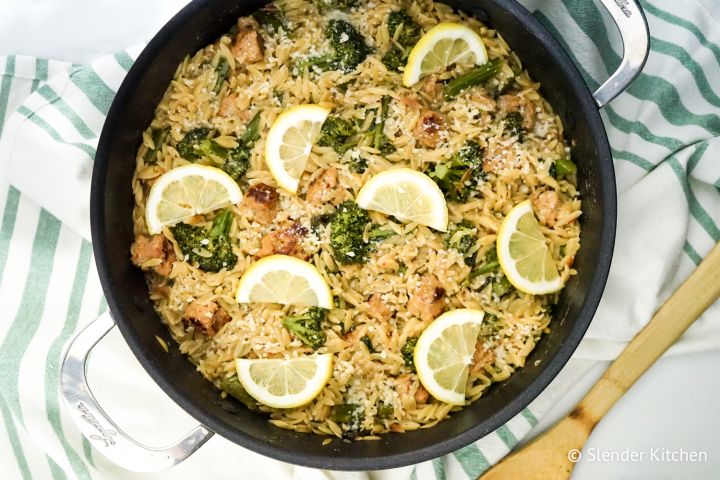 Lemon orzo cooked with chicken sausage and broccoli in a skillet.