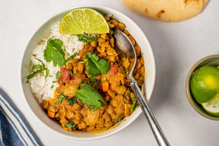 Lentil coconut curry in a white bowl with creamy lentils, carrots, and tomatoes in a creamy coconut broth with rice.