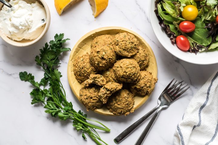 Baked lentil falafel on plate served with lemon, yogurt sauce, and salad.