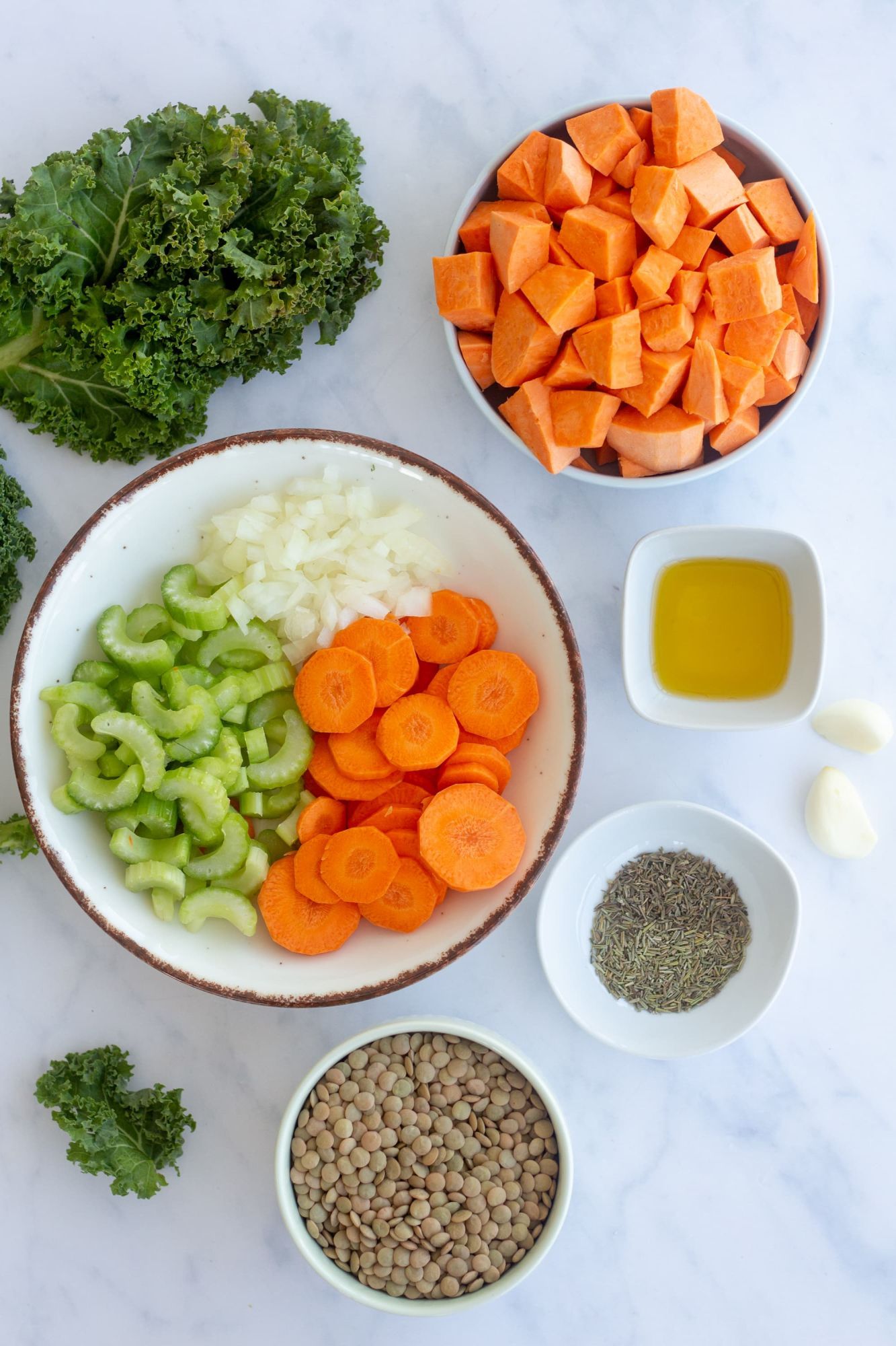 Ingredients for lentil soup including lentils, sweet potatoes, kale. lentils, celery, onion, garlic, and dried herbs,