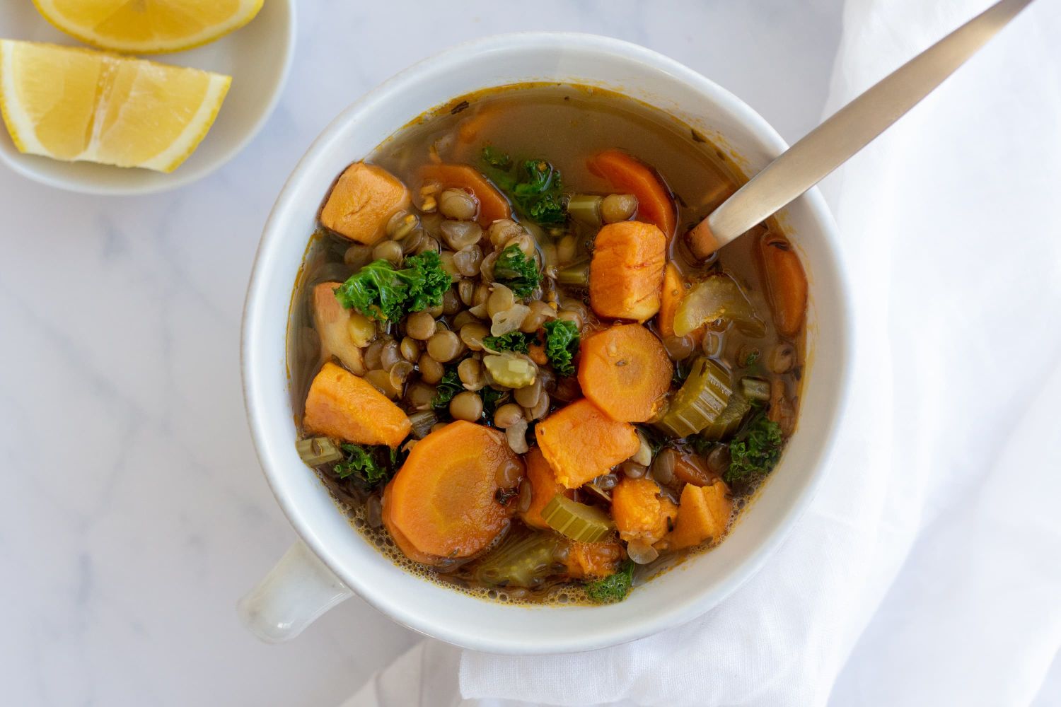 Homemade lentil soup with green lentils, vegetables, and chicken broth served in two white bowls with lemon.